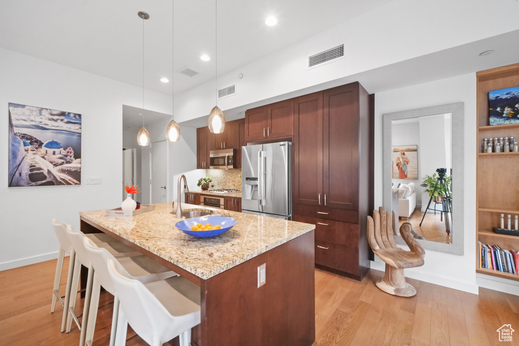 Kitchen with appliances with stainless steel finishes, light wood-style floors, a breakfast bar area, pendant lighting, and light stone countertops