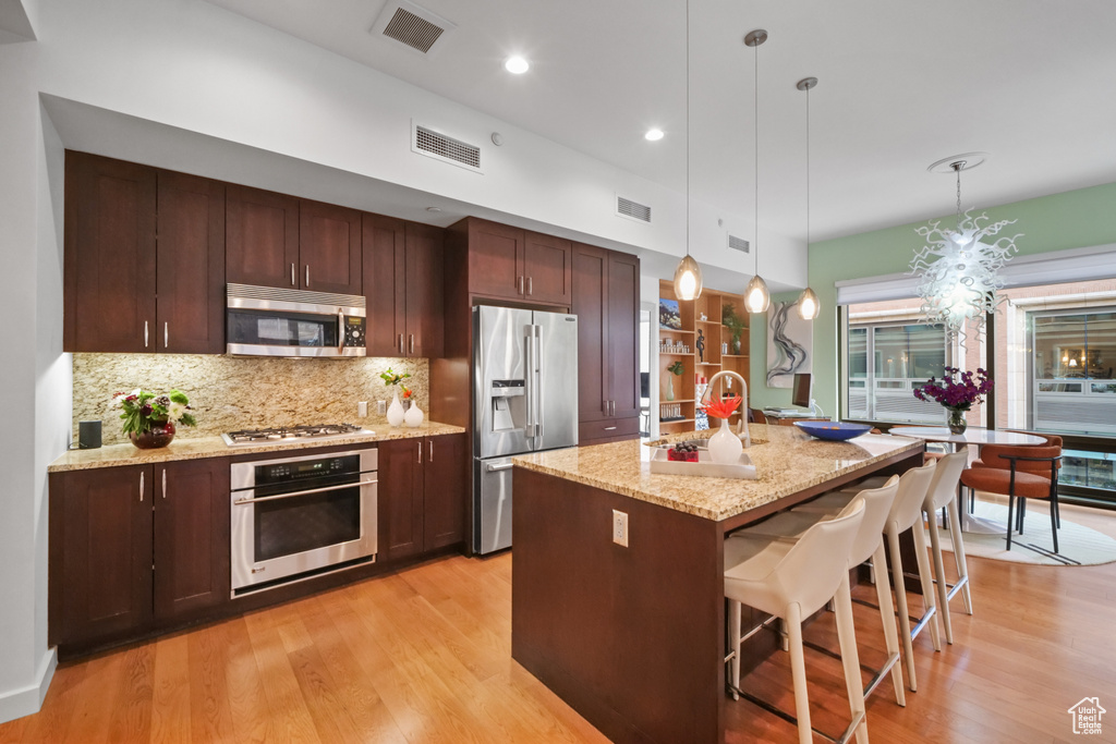 Kitchen with stainless steel appliances, light wood-type flooring, tasteful backsplash, a breakfast bar, and decorative light fixtures