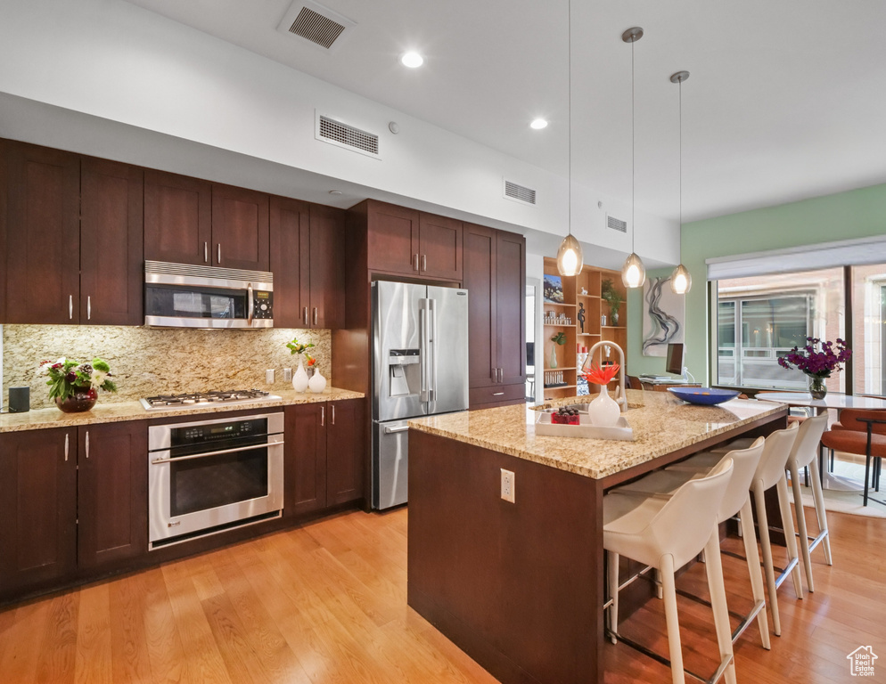 Kitchen featuring appliances with stainless steel finishes, light wood-style floors, backsplash, a kitchen bar, and recessed lighting