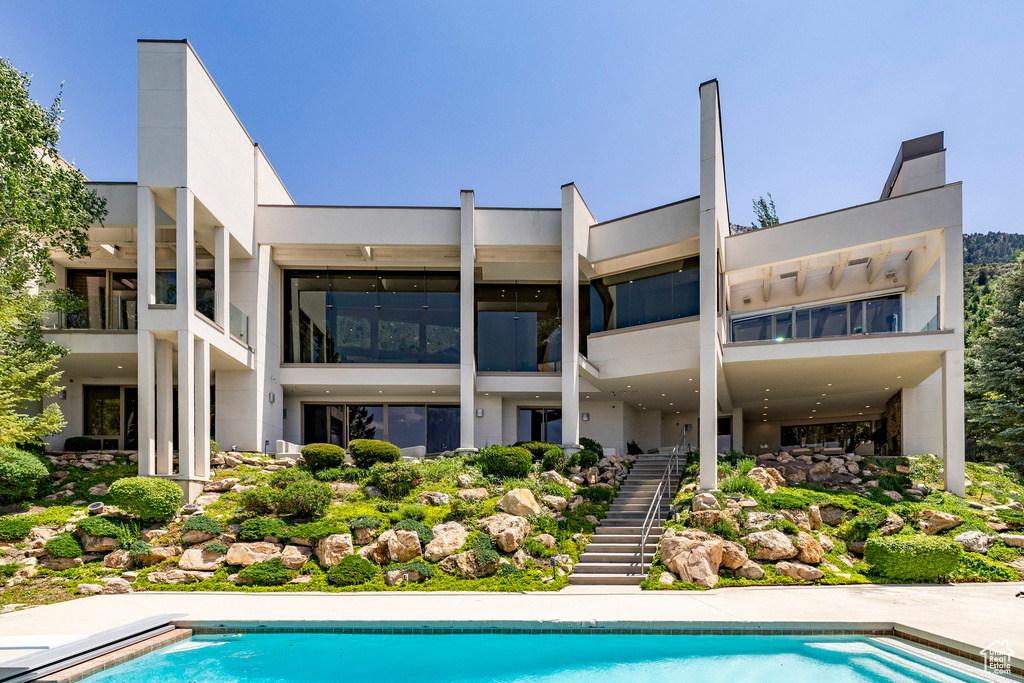 Rear view of house with stairs, an outdoor pool, and stucco siding