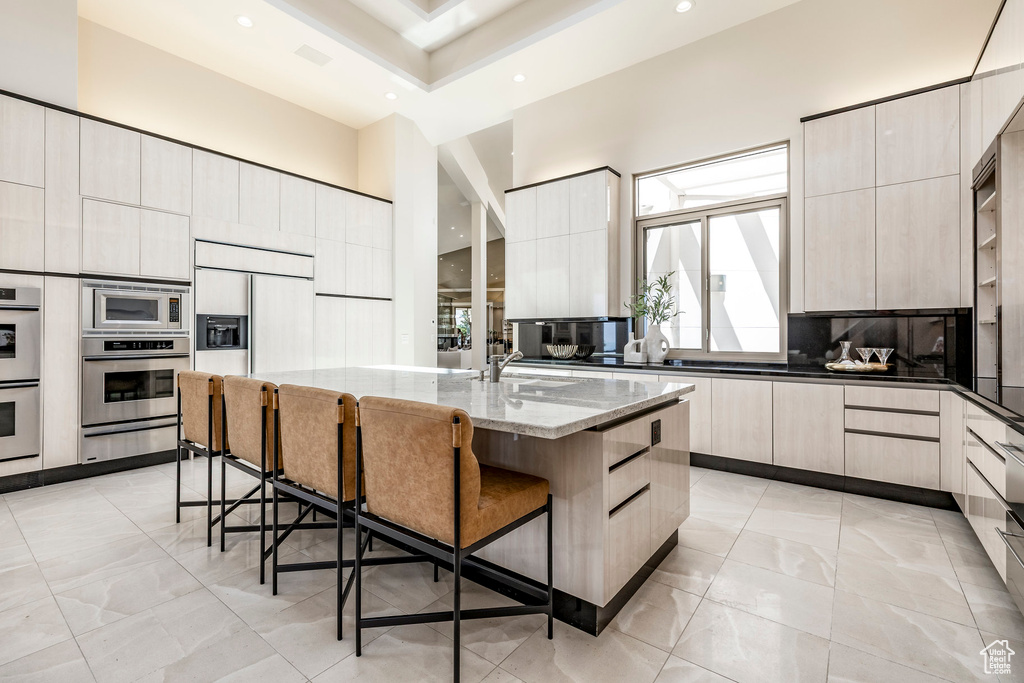 Kitchen with modern cabinets, a warming drawer, light stone counters, recessed lighting, and a breakfast bar area