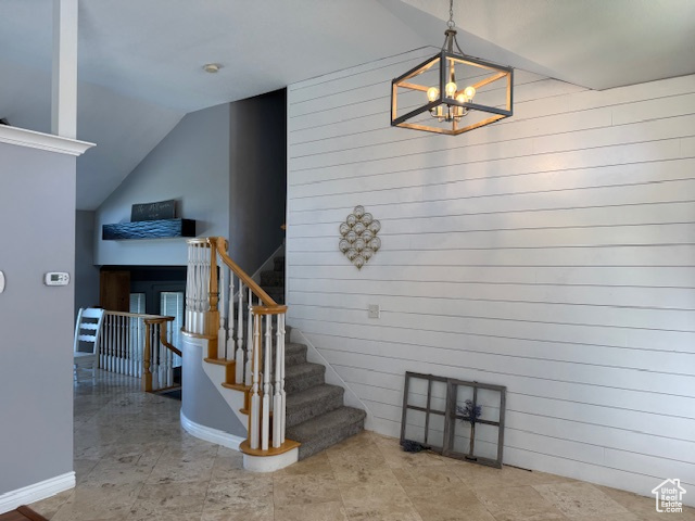 Staircase featuring vaulted ceiling, a chandelier, and wood walls
