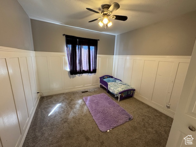 Unfurnished bedroom with a decorative wall, carpet flooring, a wainscoted wall, and ceiling fan