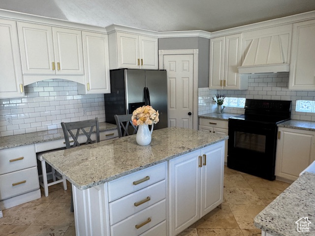 Kitchen with black / electric stove, stainless steel refrigerator with ice dispenser, custom exhaust hood, white cabinetry, and light stone countertops