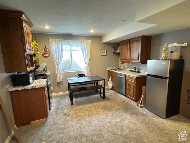 Kitchen with stainless steel appliances, light colored carpet, light countertops, brown cabinetry, and a textured ceiling