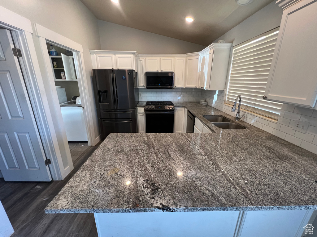 Kitchen featuring appliances with stainless steel finishes, vaulted ceiling, dark stone counters, white cabinets, and dark wood-style floors