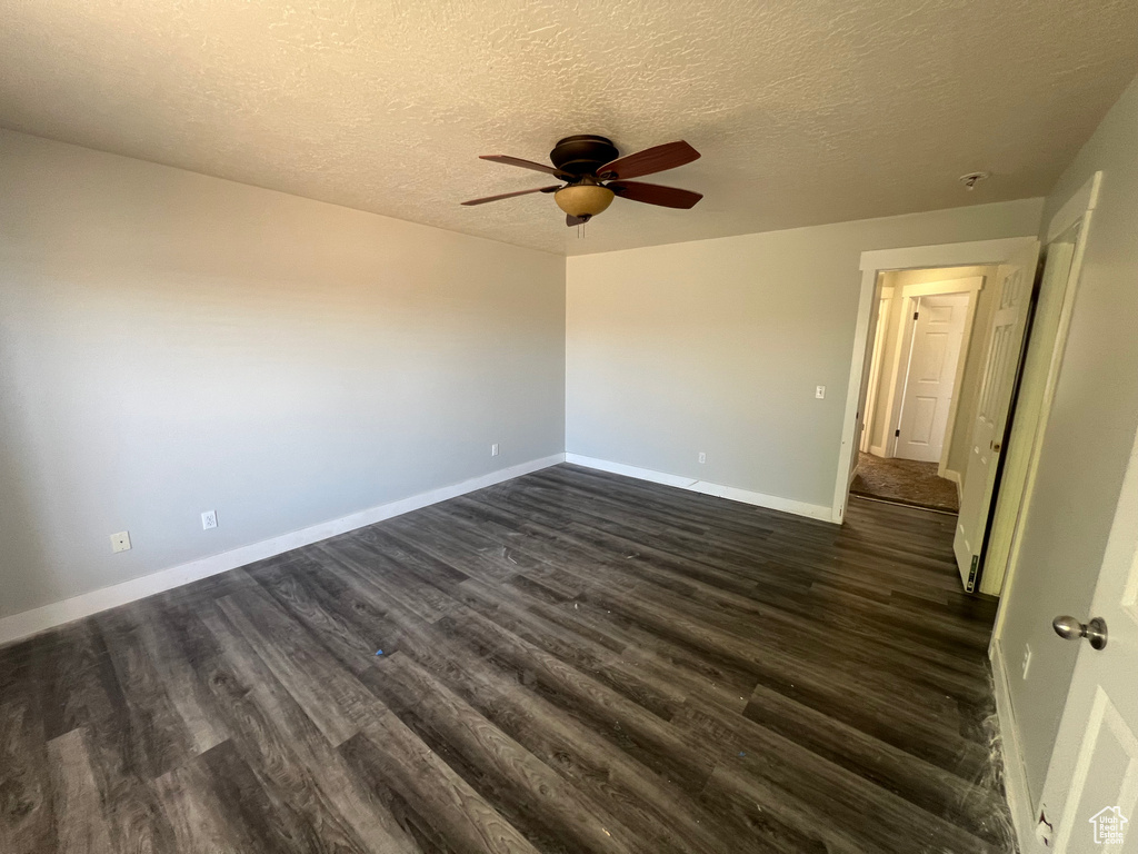 Empty room featuring a ceiling fan, dark wood-style flooring, and a textured ceiling