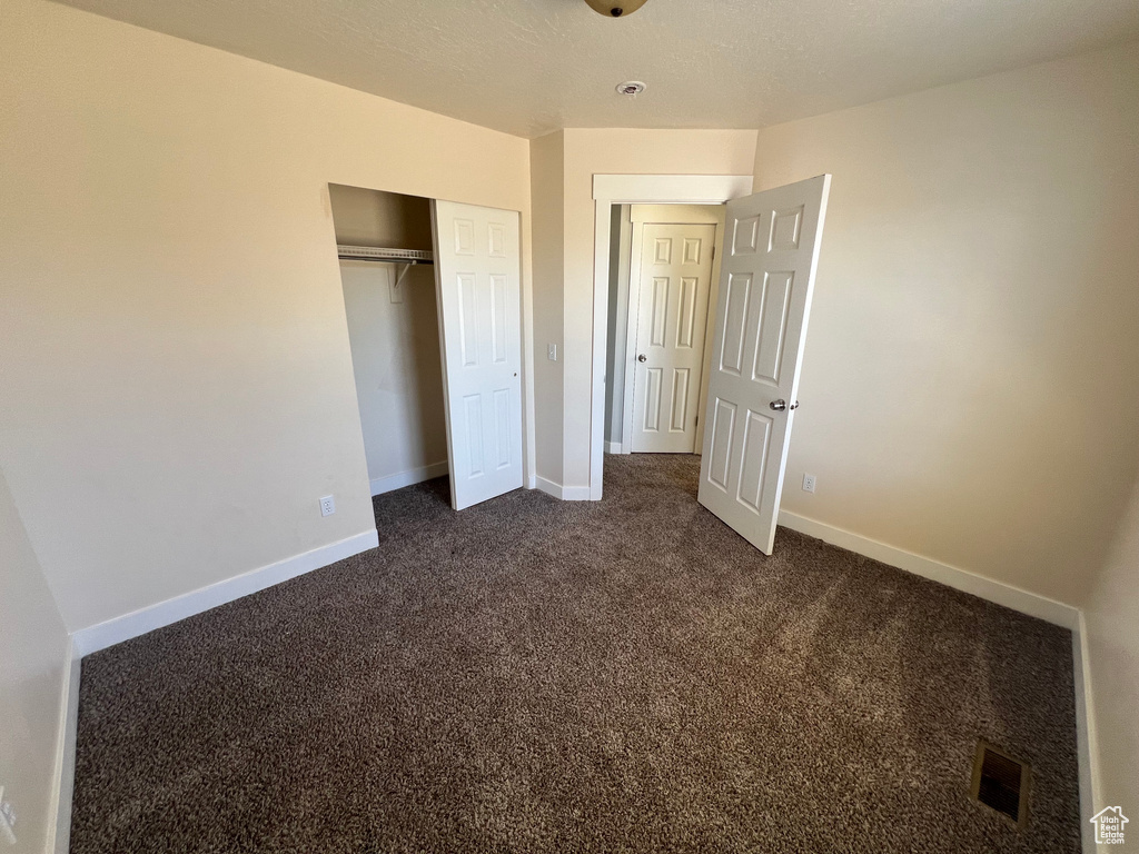 Unfurnished bedroom with dark carpet and a closet