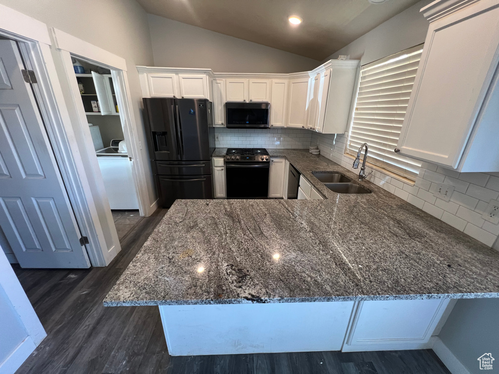 Kitchen with stainless steel appliances, vaulted ceiling, dark stone counters, white cabinetry, and a peninsula