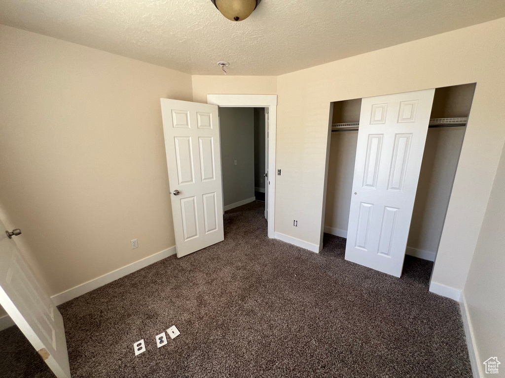 Unfurnished bedroom with dark carpet, a closet, and a textured ceiling