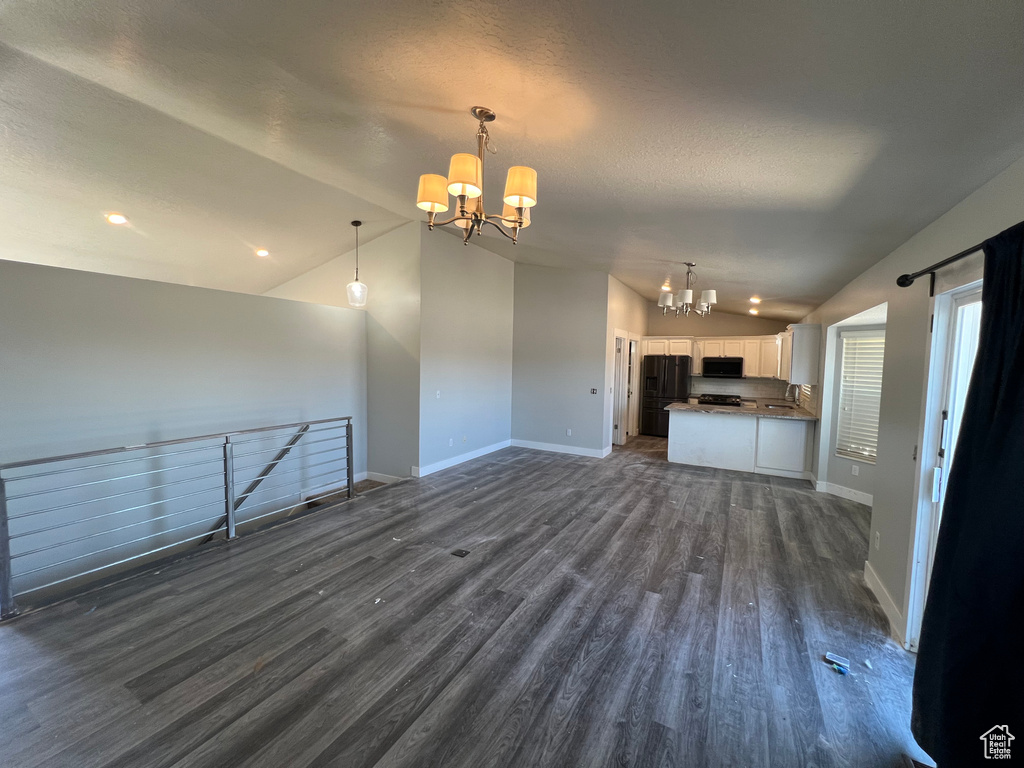 Unfurnished living room featuring a chandelier, vaulted ceiling, dark wood-type flooring, a textured ceiling, and recessed lighting