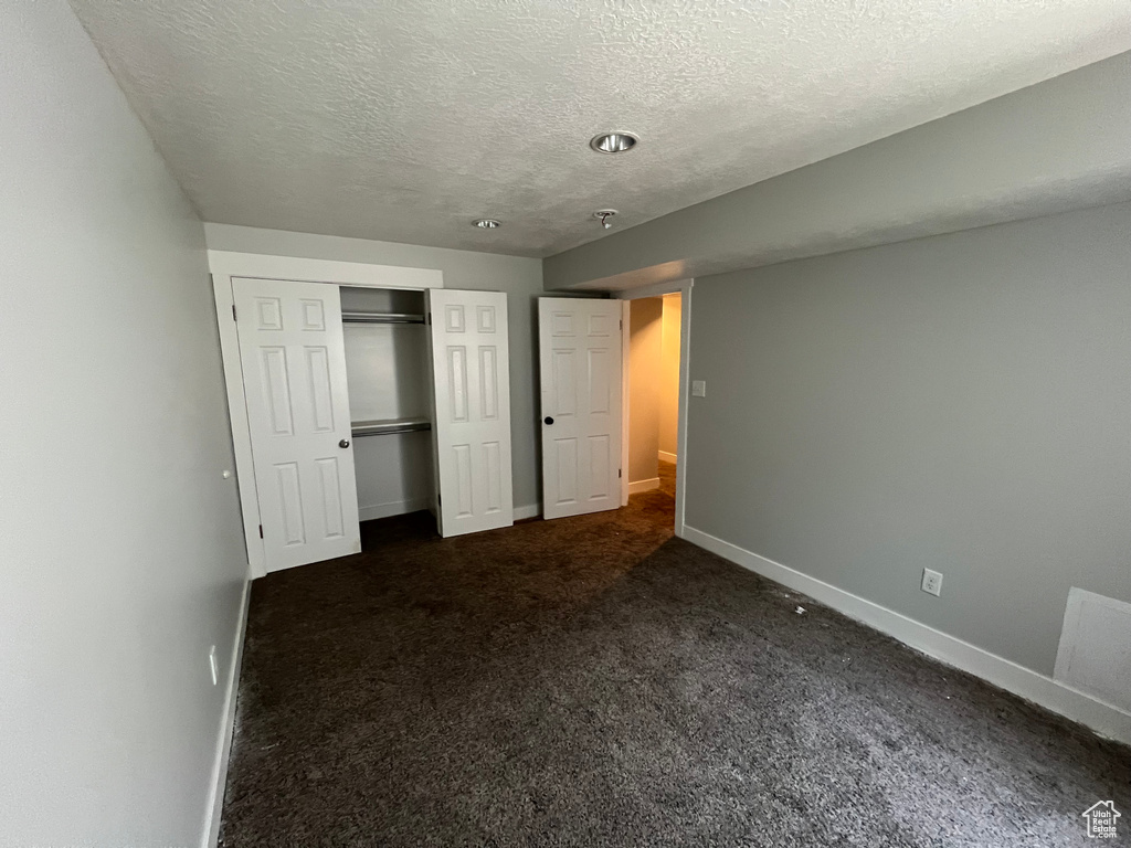 Unfurnished bedroom with a textured ceiling, dark colored carpet, and a closet