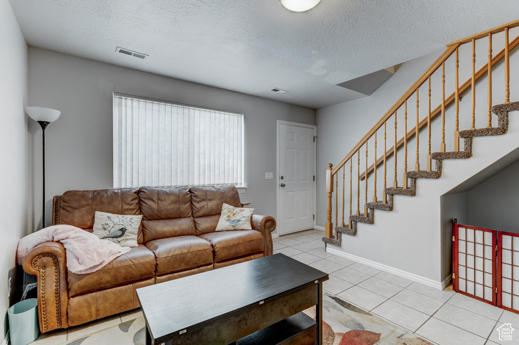 Living room with stairway, light tile patterned flooring, and a textured ceiling