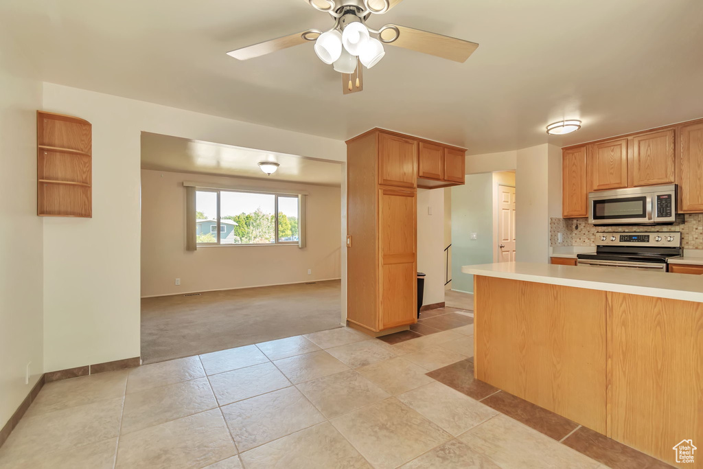 Kitchen with stainless steel appliances, light countertops, decorative backsplash, ceiling fan, and light tile patterned floors