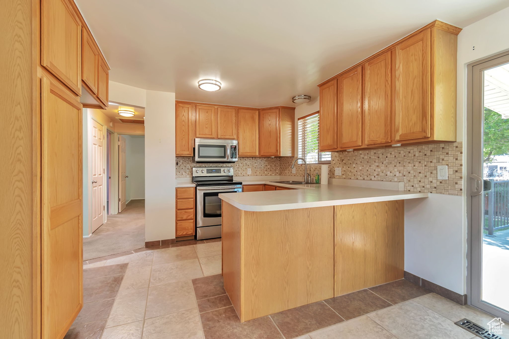 Kitchen featuring appliances with stainless steel finishes, a peninsula, tasteful backsplash, light countertops, and light tile patterned floors