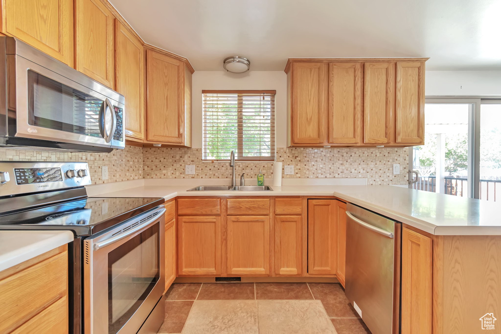 Kitchen with appliances with stainless steel finishes, a peninsula, light countertops, and backsplash