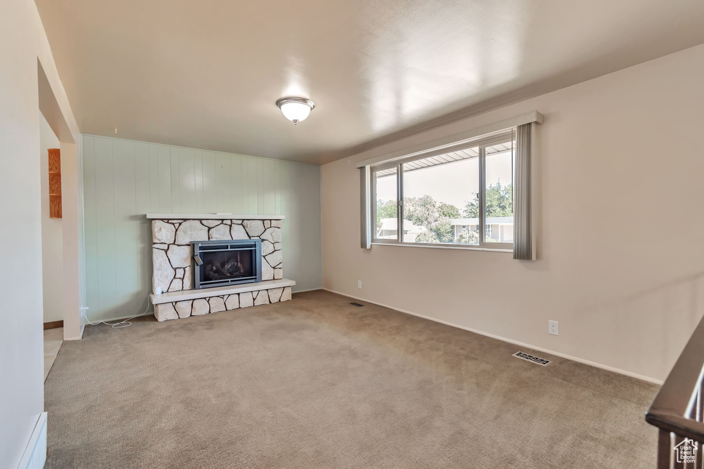Unfurnished living room with carpet, a stone fireplace, and a baseboard radiator