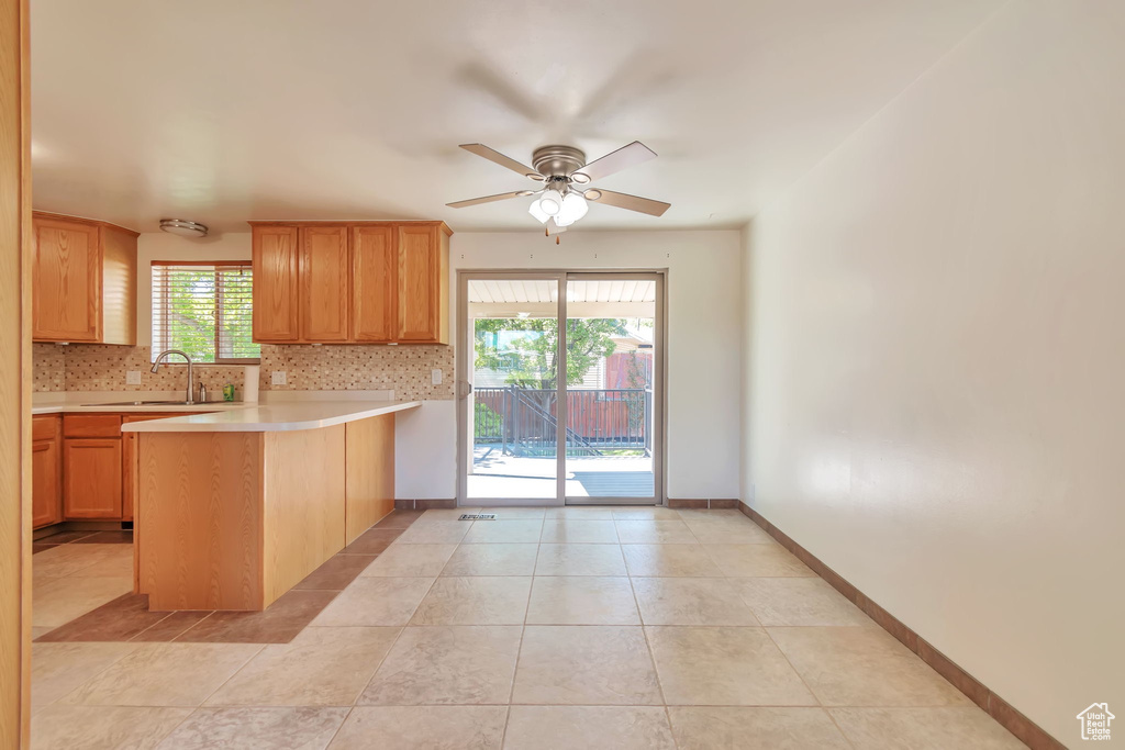 Kitchen featuring a peninsula, light countertops, tasteful backsplash, ceiling fan, and light tile patterned floors