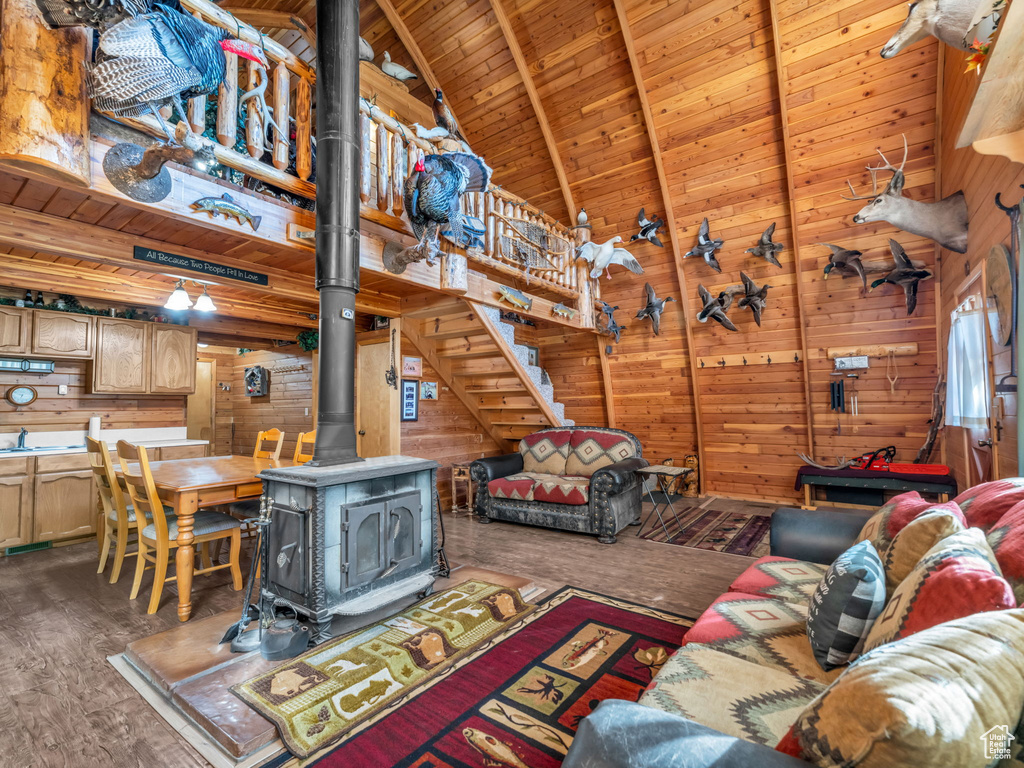 Living area featuring wooden walls, a wood ceiling with exposed beams, a wood stove, wood finished floors, and high vaulted ceiling