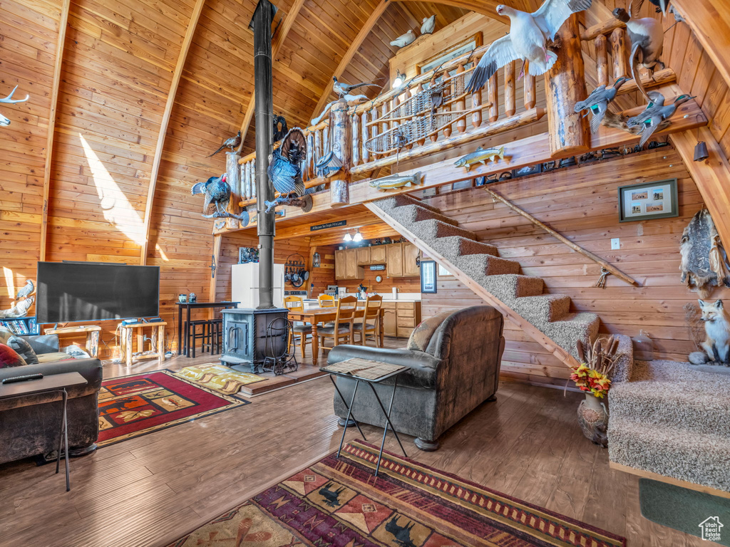 Living room with wooden walls, high vaulted ceiling, a wood stove, hardwood / wood-style floors, and a wooden ceiling with exposed beams
