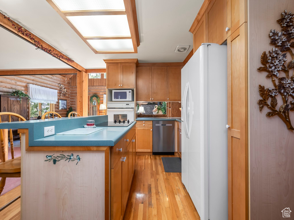 Kitchen featuring white appliances, light wood finished floors, a kitchen breakfast bar, backsplash, and log walls