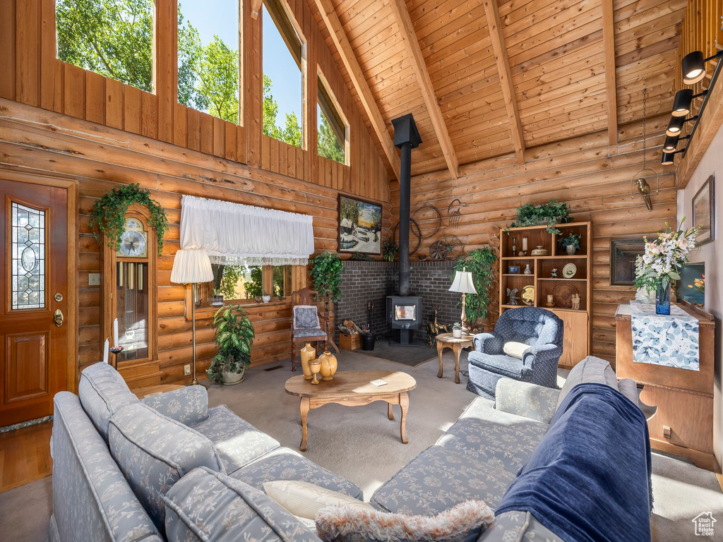 Carpeted living area featuring a wood stove, log walls, high vaulted ceiling, and a wood ceiling with exposed beams