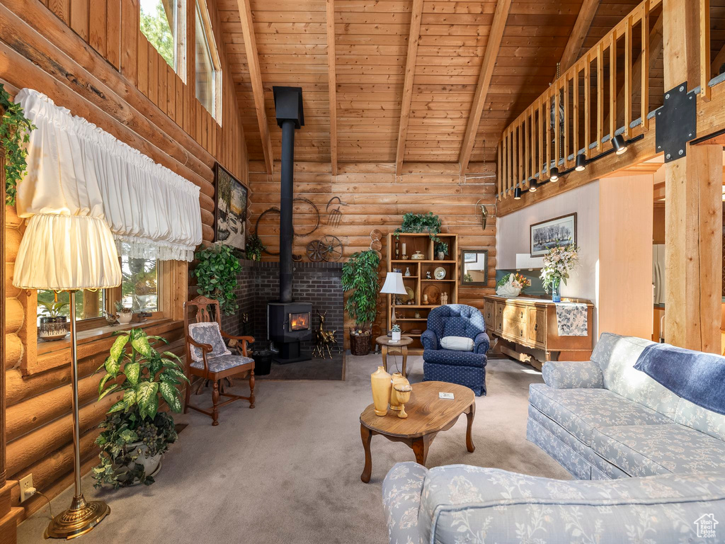 Living room with a wood stove, carpet, log walls, a wood ceiling with exposed beams, and high vaulted ceiling