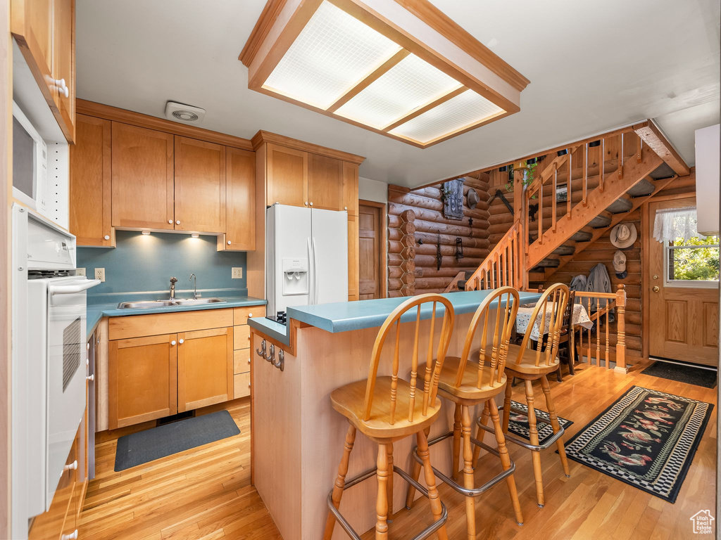 Kitchen featuring rustic walls, white appliances, light wood-style floors, and a breakfast bar area
