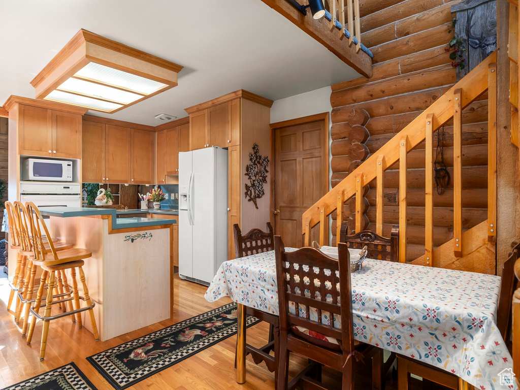 Kitchen with white appliances, rustic walls, light wood finished floors, a kitchen breakfast bar, and dark countertops