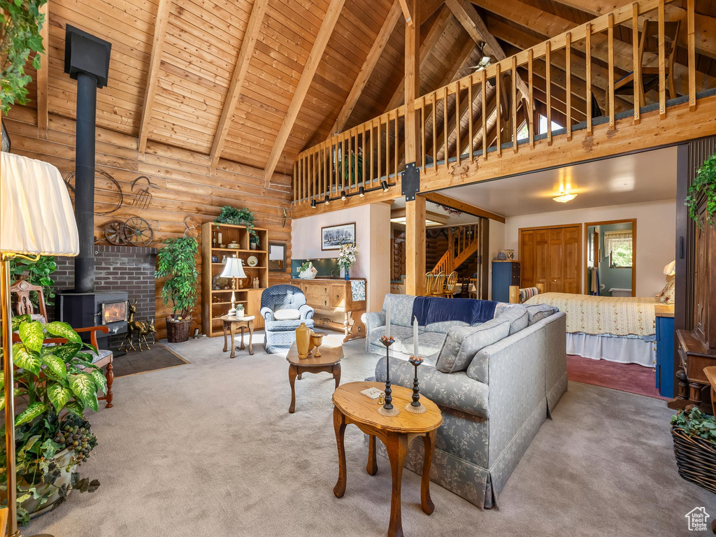 Carpeted living area featuring a wood stove, high vaulted ceiling, and a wood ceiling with exposed beams