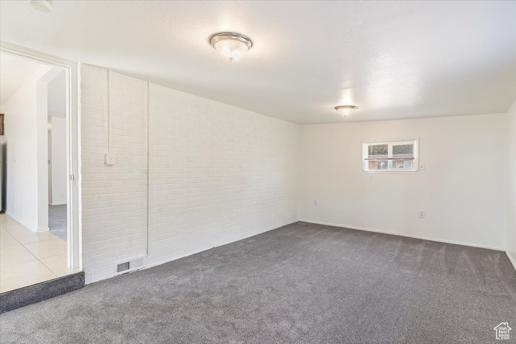 Carpeted empty room featuring brick wall and baseboards