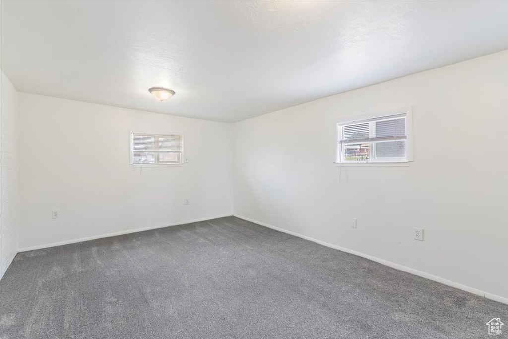 Unfurnished room with plenty of natural light and dark colored carpet