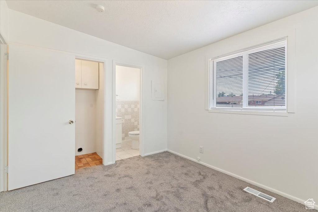Unfurnished bedroom featuring light carpet, light tile patterned flooring, and ensuite bathroom