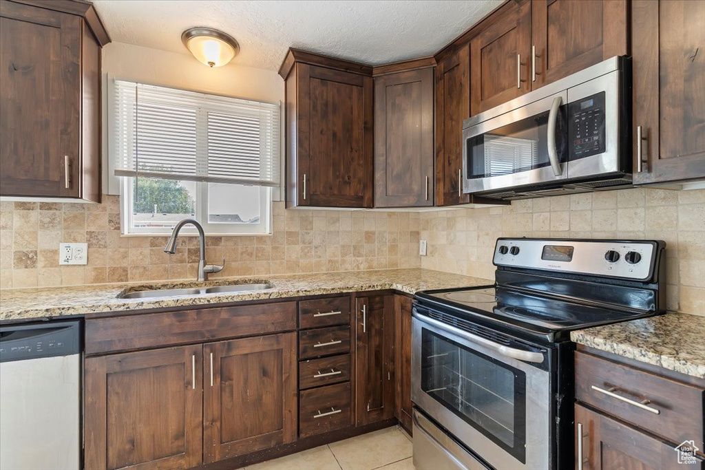 Kitchen with appliances with stainless steel finishes, light stone countertops, decorative backsplash, light tile patterned floors, and dark brown cabinets