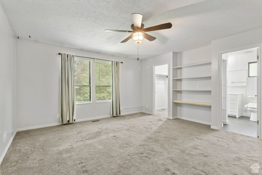Unfurnished bedroom with a textured ceiling, carpet, a spacious closet, connected bathroom, and a ceiling fan