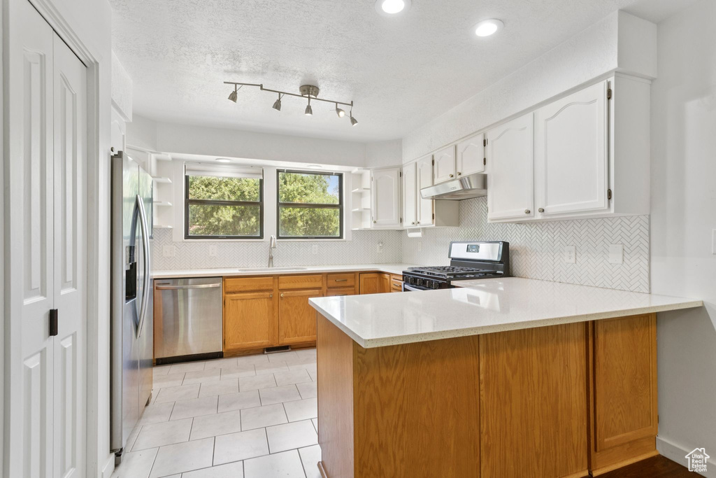 Kitchen with appliances with stainless steel finishes, under cabinet range hood, a peninsula, open shelves, and backsplash
