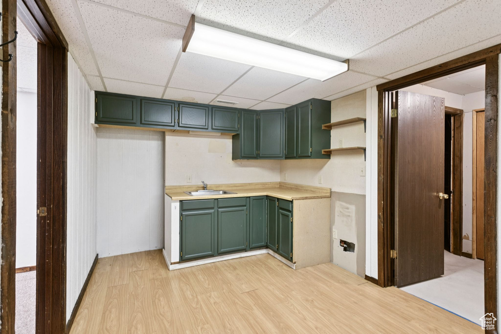 Kitchen featuring green cabinetry, light wood-type flooring, a drop ceiling, open shelves, and light countertops