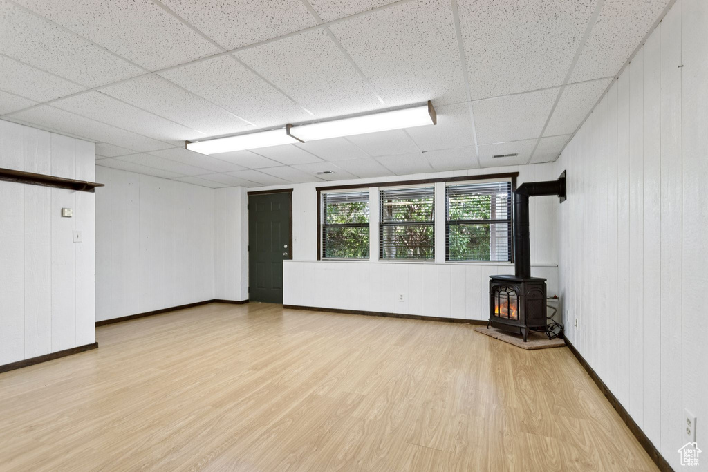 Unfurnished living room with a wood stove, light wood-type flooring, a drop ceiling, and wood walls