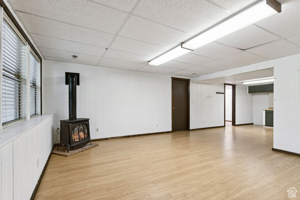 Unfurnished living room featuring light wood finished floors, a wood stove, and a paneled ceiling