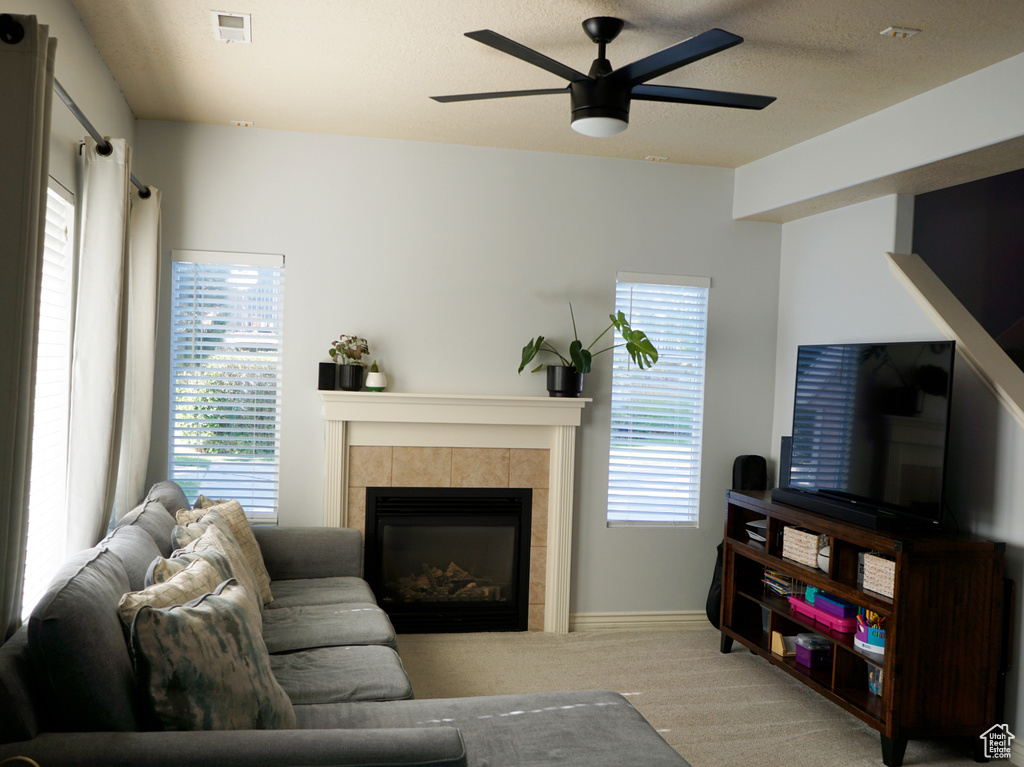 Carpeted living room featuring ceiling fan, a tile fireplace, and plenty of natural light