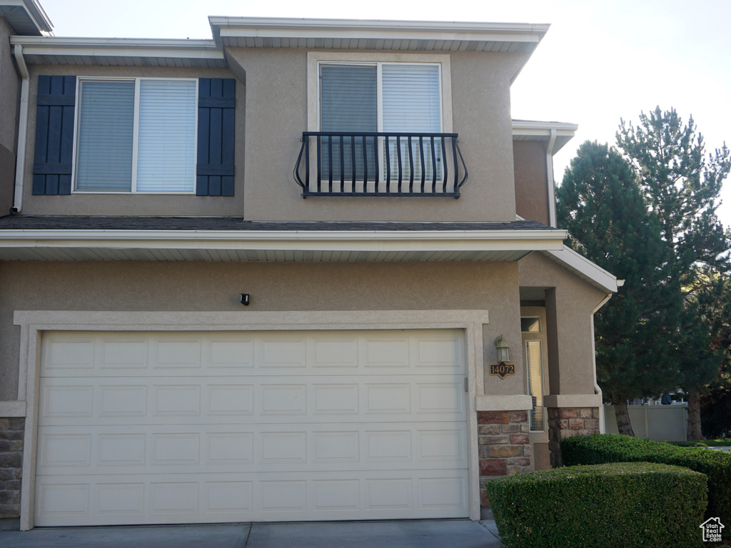 View of front facade with an attached garage, stucco siding, stone siding, and concrete driveway