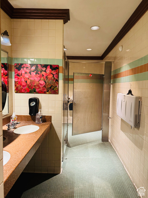 Full bath with tile walls, crown molding, tile patterned floors, a shower stall, and double vanity