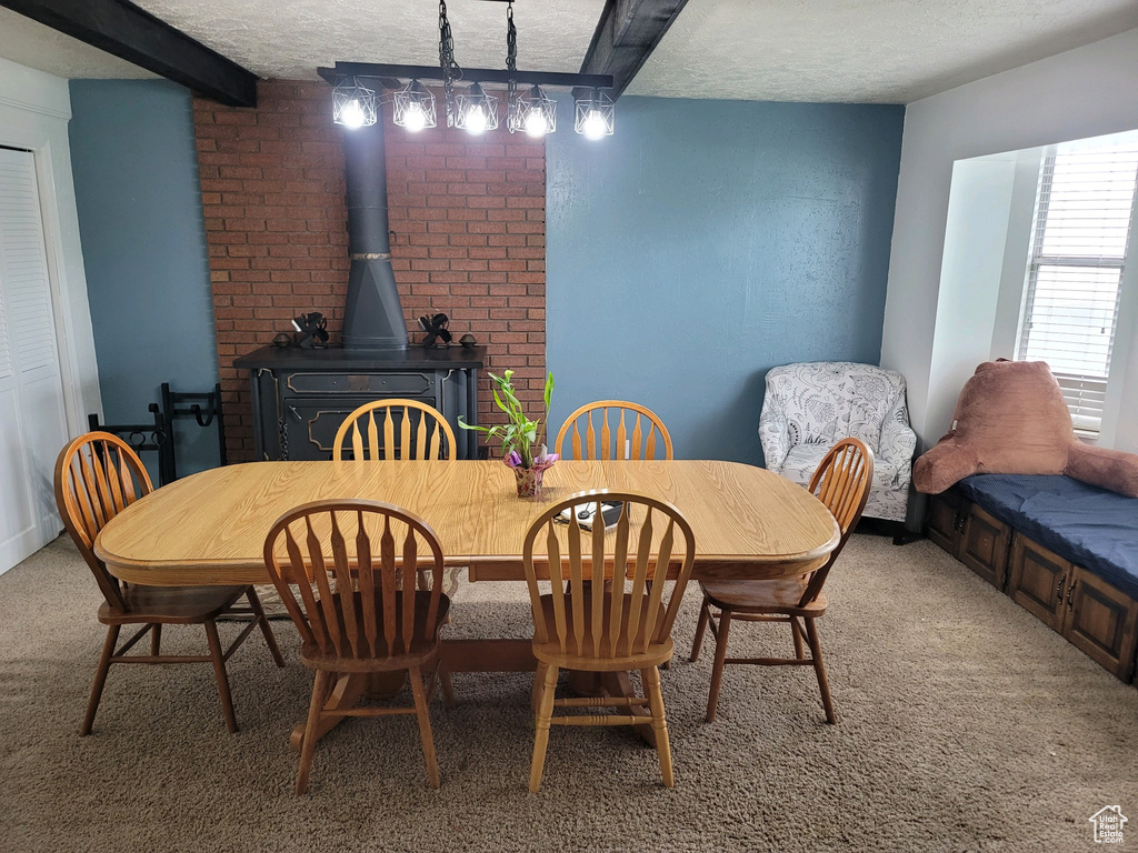 Dining space with light colored carpet, a textured ceiling, a wood stove, and beam ceiling