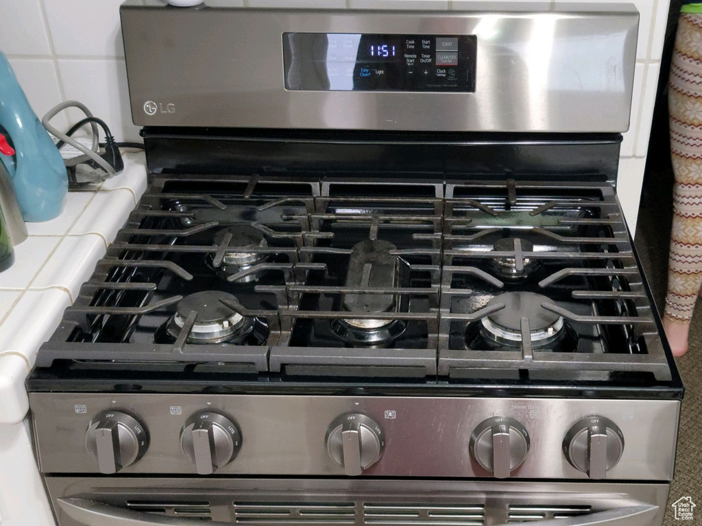 Kitchen view of tile countertops, stainless steel gas range, white cabinets, and backsplash