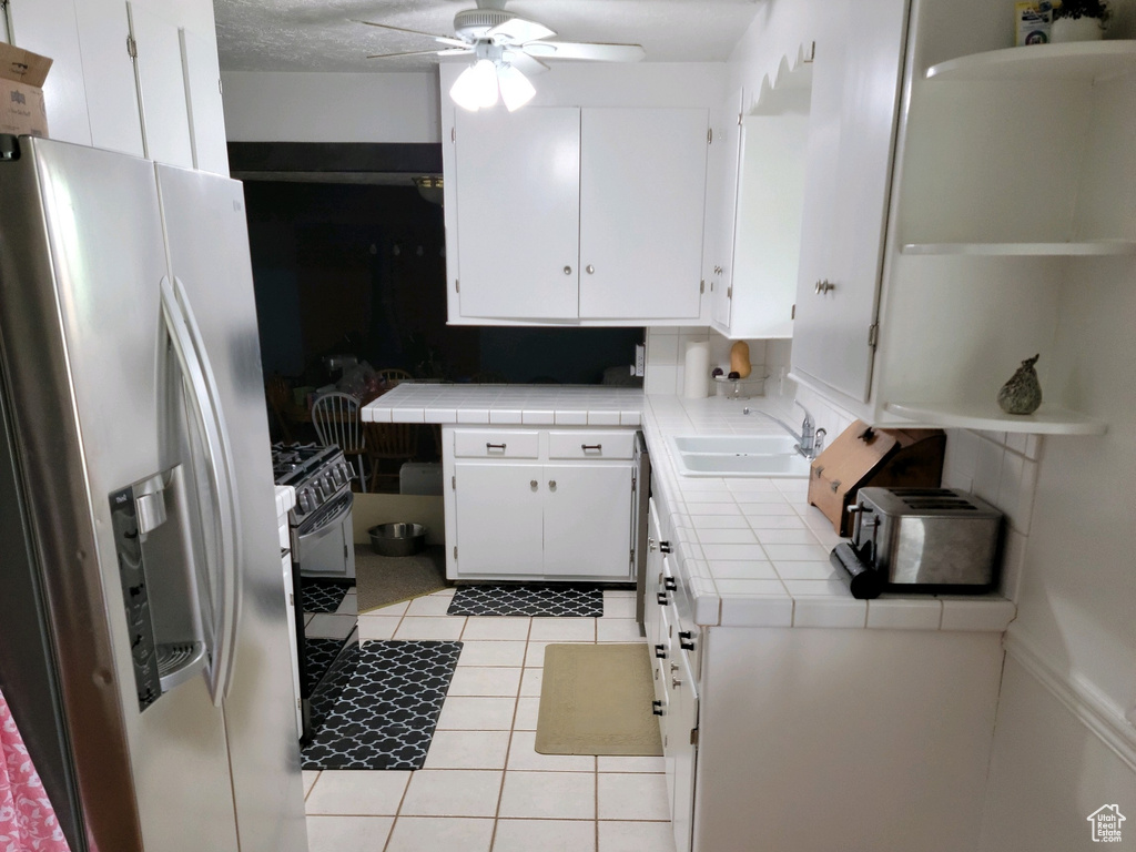 Kitchen with appliances with stainless steel finishes, tile counters, a ceiling fan, light wood-style floors, and white cabinetry