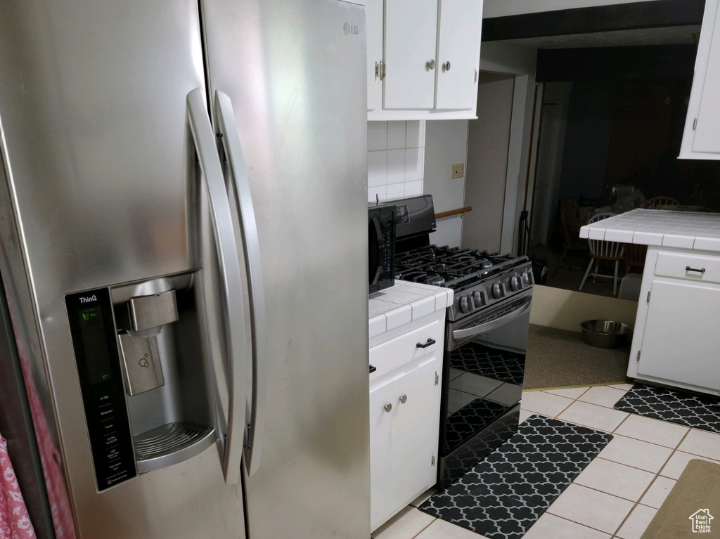 Kitchen featuring appliances with stainless steel finishes, tile countertops, light tile patterned flooring, and white cabinetry