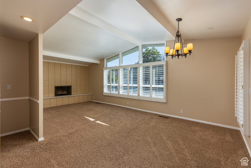 Unfurnished living room with carpet floors, a chandelier, and a brick fireplace