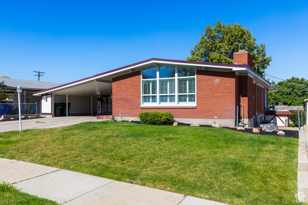 Mid-century inspired home featuring driveway, an attached carport, a chimney, a front lawn, and brick siding