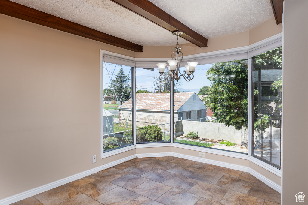 Unfurnished sunroom featuring beam ceiling and a chandelier