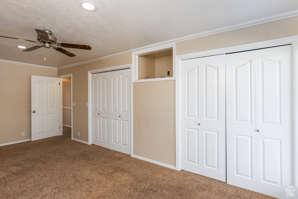 Unfurnished bedroom featuring carpet floors, crown molding, two closets, and ceiling fan